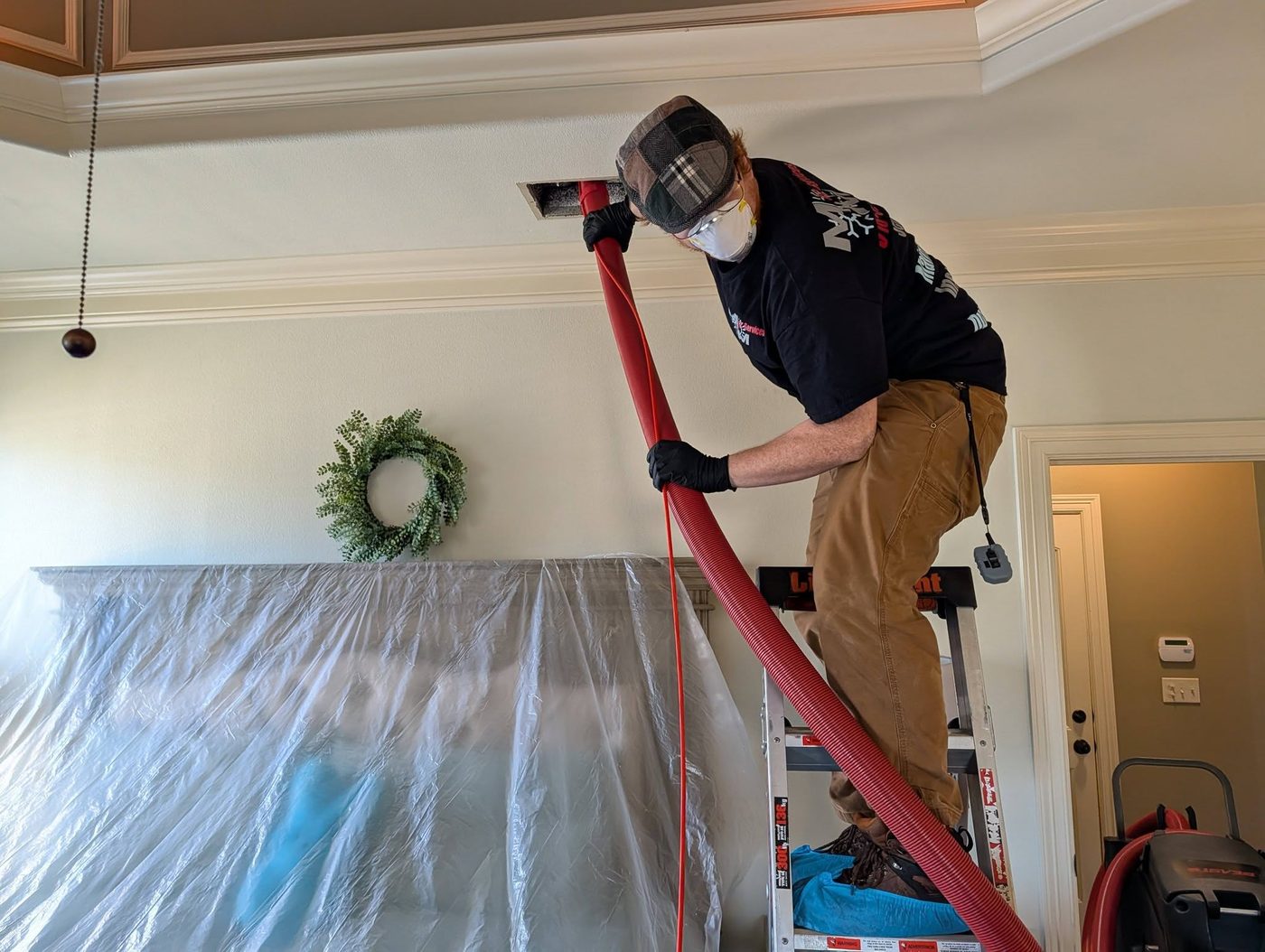 M-n-M technician cleaning a ceiling air duct with a vacuum hose