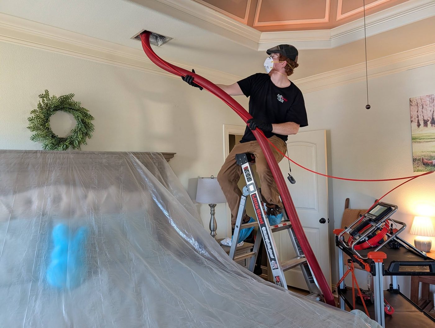 M-n-M technician on a ladder cleaning a ceiling vent